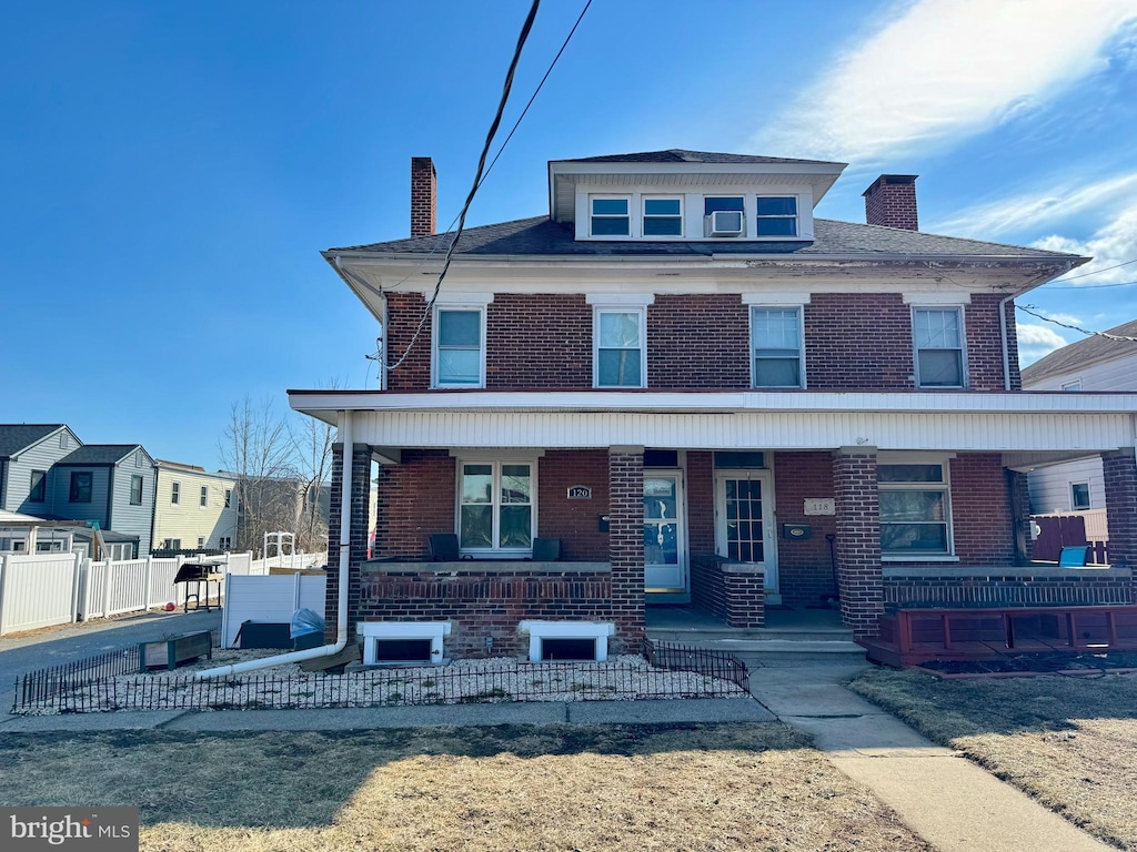 american foursquare style home featuring a porch, brick siding, and a chimney