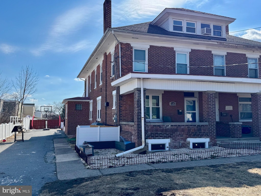 american foursquare style home featuring a chimney, fence, a porch, and brick siding