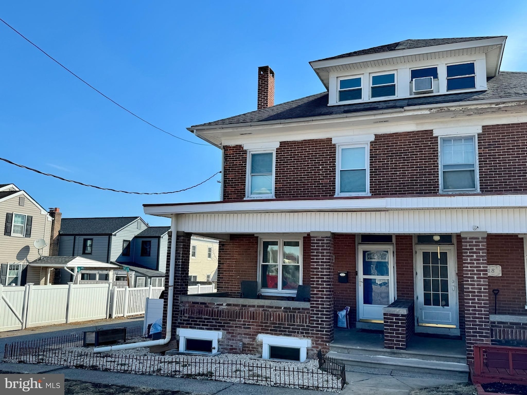 traditional style home featuring covered porch, brick siding, a chimney, and fence