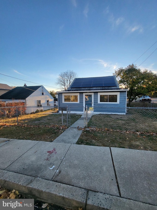 bungalow-style house with solar panels, a front lawn, and a fenced front yard