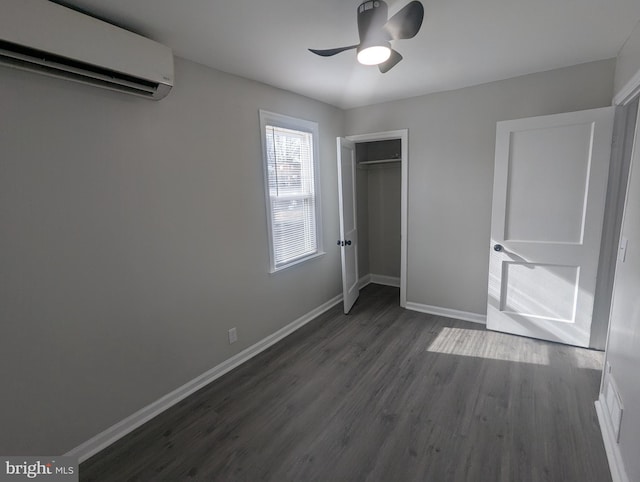 unfurnished bedroom featuring a wall unit AC, dark wood finished floors, a closet, ceiling fan, and baseboards