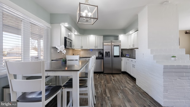 kitchen with dark wood-type flooring, white cabinets, hanging light fixtures, appliances with stainless steel finishes, and dark countertops