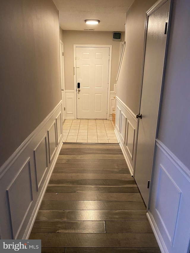 corridor with dark wood-style flooring, a wainscoted wall, and a decorative wall