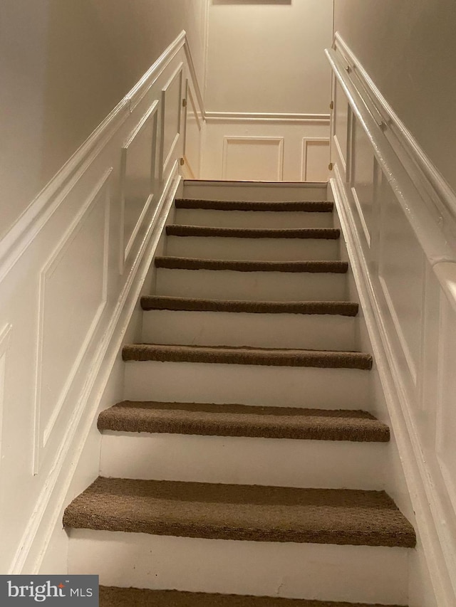 stairway with wainscoting and a decorative wall