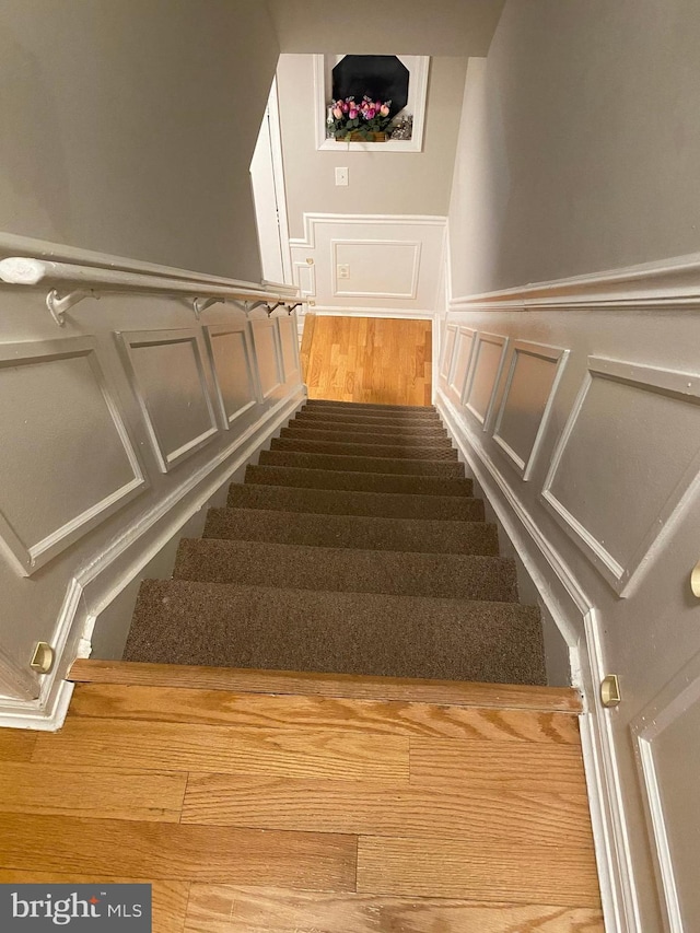 stairway with a wainscoted wall, wood finished floors, and a decorative wall