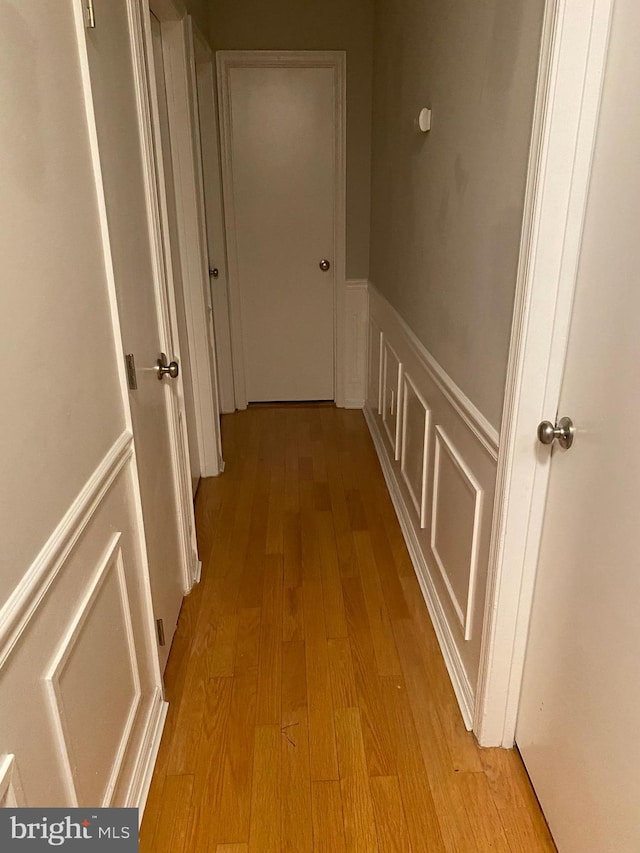 hall featuring light wood-style floors, a decorative wall, and wainscoting