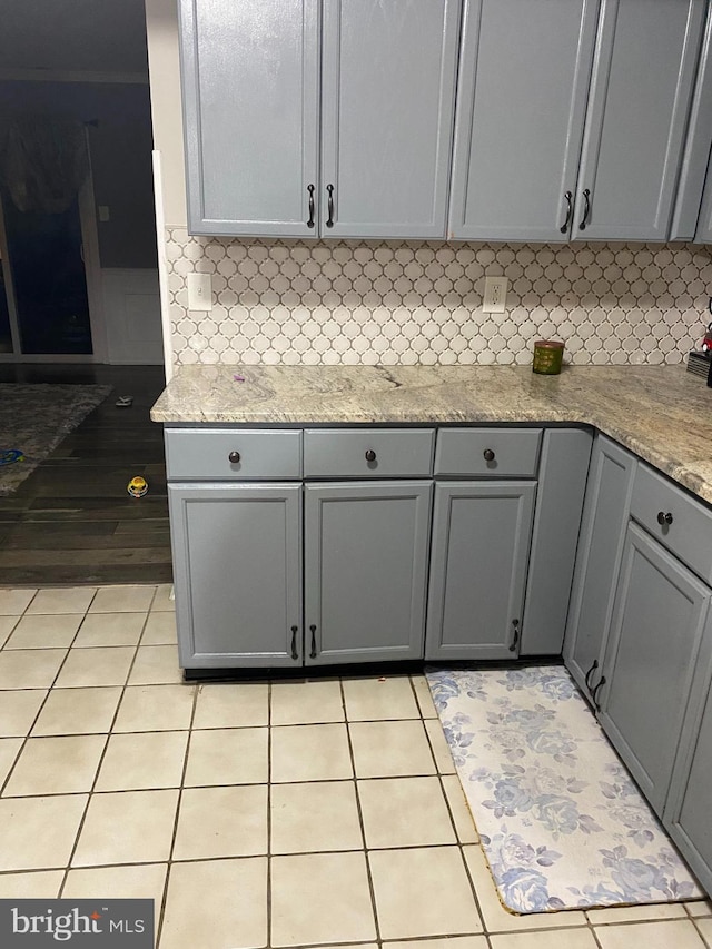 kitchen with light tile patterned floors, tasteful backsplash, light stone counters, and gray cabinets