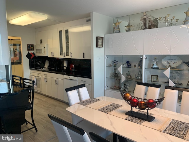 kitchen featuring glass insert cabinets, dark countertops, white appliances, and white cabinetry