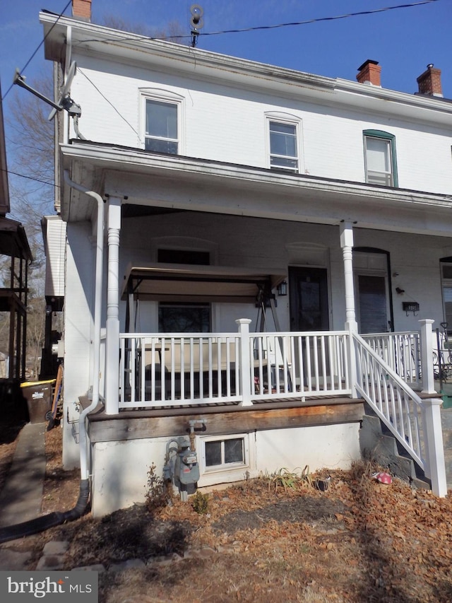 view of front of house featuring a chimney, a porch, and brick siding