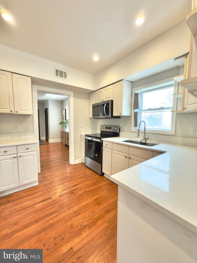 kitchen with visible vents, a sink, appliances with stainless steel finishes, white cabinetry, and light wood-type flooring