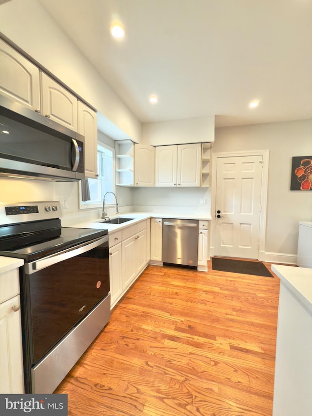 kitchen featuring open shelves, light countertops, appliances with stainless steel finishes, light wood-style floors, and a sink