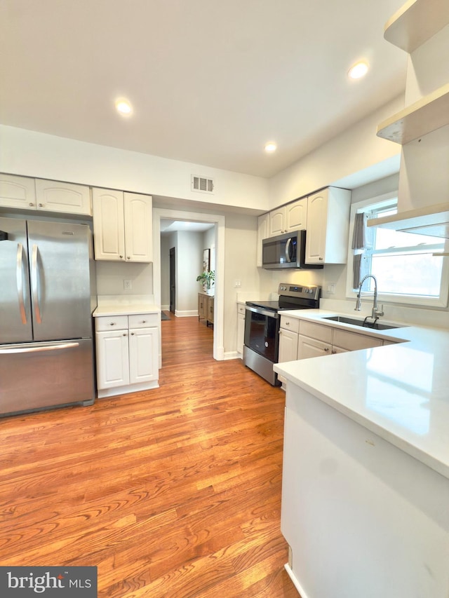 kitchen featuring visible vents, a sink, stainless steel appliances, light countertops, and light wood-type flooring