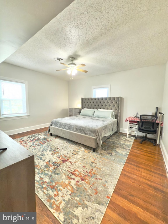 bedroom featuring baseboards, multiple windows, visible vents, and wood finished floors