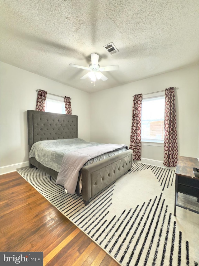 bedroom featuring visible vents, multiple windows, baseboards, and wood finished floors