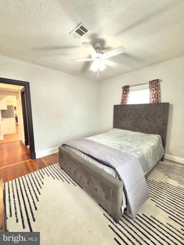 bedroom with visible vents, a ceiling fan, a textured ceiling, wood finished floors, and baseboards