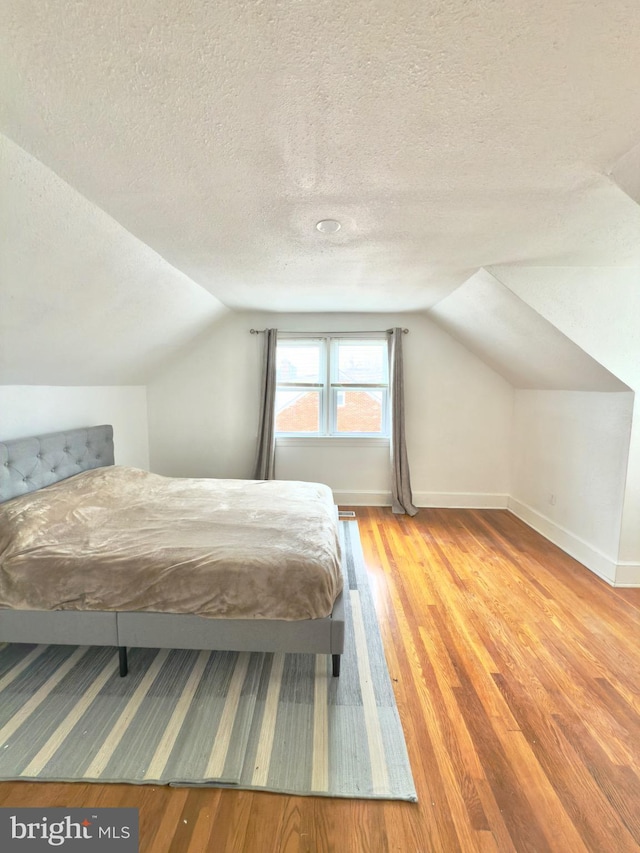 unfurnished bedroom with vaulted ceiling, wood finished floors, baseboards, and a textured ceiling