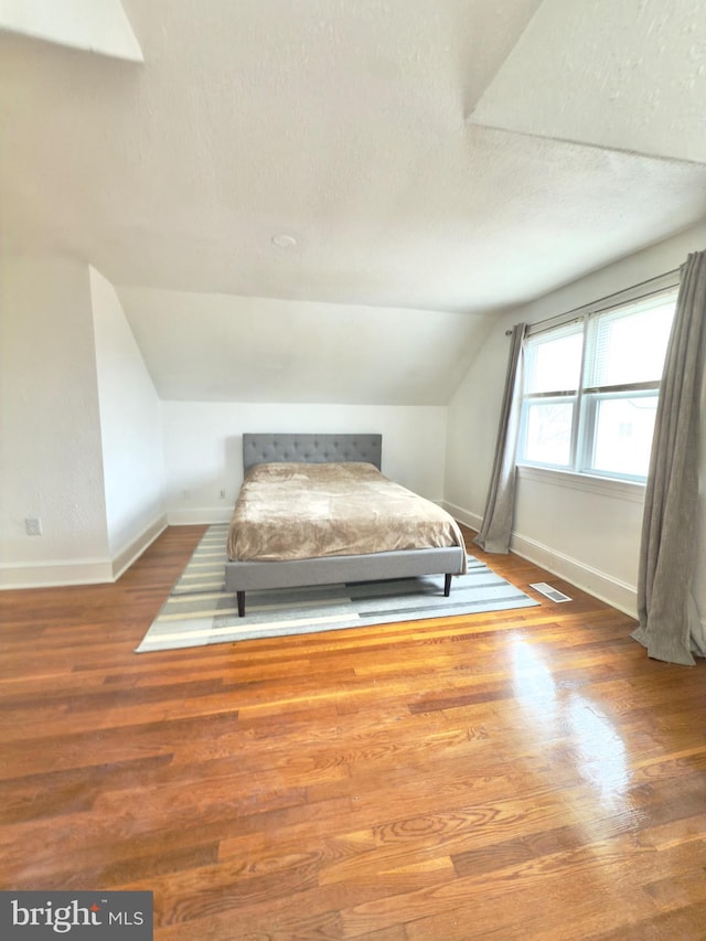 unfurnished bedroom with vaulted ceiling, visible vents, baseboards, and wood finished floors