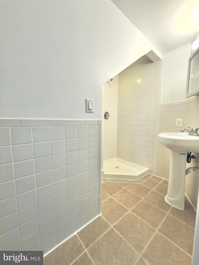 full bathroom with tile patterned flooring, wainscoting, a tile shower, and tile walls