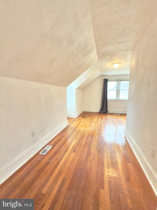 bonus room featuring visible vents, baseboards, vaulted ceiling, wood finished floors, and a textured ceiling