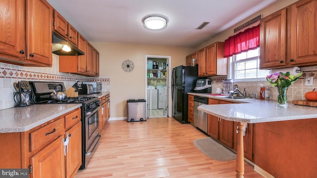 kitchen featuring visible vents, washer and clothes dryer, appliances with stainless steel finishes, light wood-type flooring, and under cabinet range hood