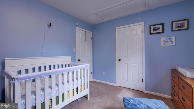 bedroom featuring light carpet, a crib, attic access, and baseboards