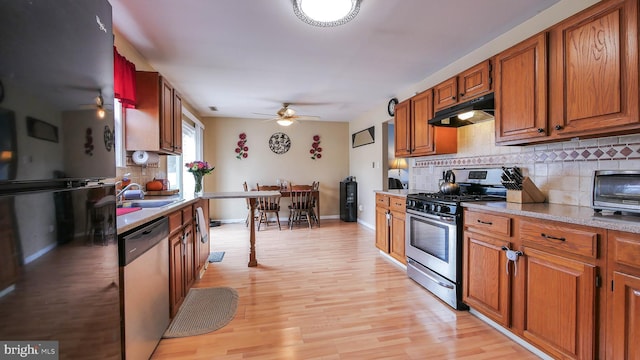 kitchen featuring under cabinet range hood, stainless steel appliances, a sink, light countertops, and tasteful backsplash