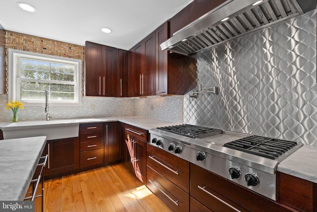 kitchen featuring a sink, light countertops, wall chimney range hood, light wood finished floors, and stainless steel gas stovetop