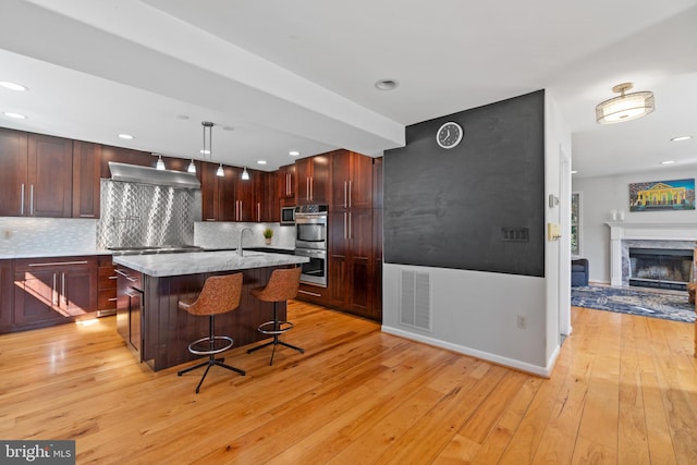 kitchen featuring visible vents, ventilation hood, a kitchen bar, a center island with sink, and pendant lighting