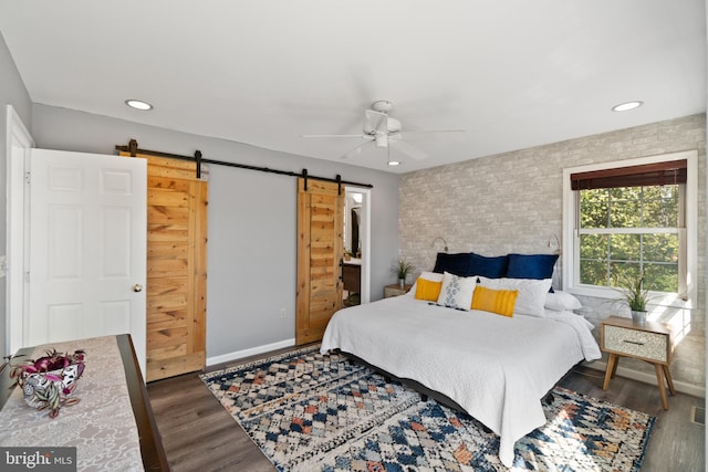 bedroom featuring dark wood finished floors, recessed lighting, a barn door, brick wall, and baseboards