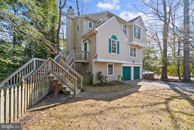 view of property exterior with a garage, fence, stairs, concrete driveway, and a chimney