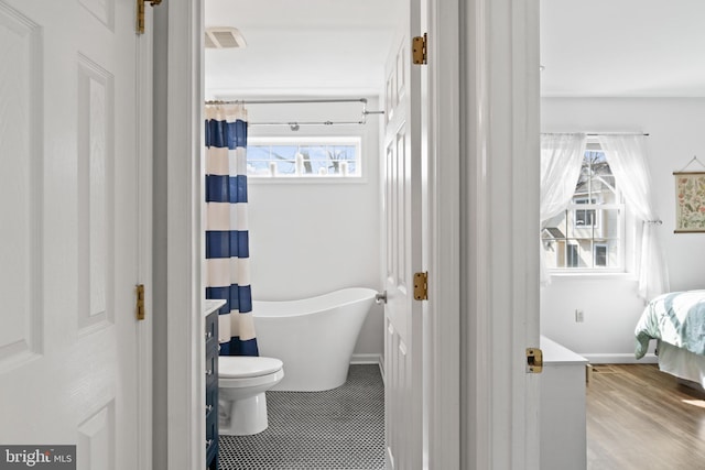 bathroom featuring toilet, a freestanding tub, baseboards, and visible vents