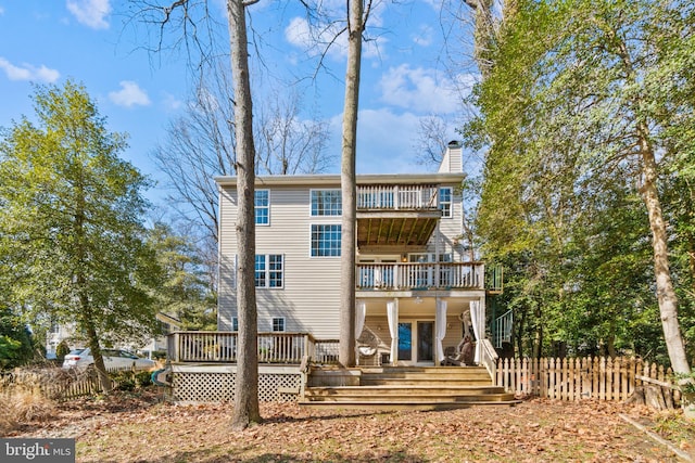 back of house with a chimney, fence, and a balcony