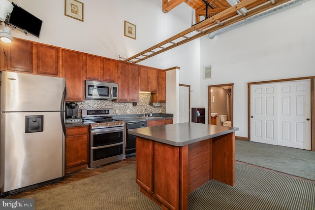 kitchen featuring a towering ceiling, dark countertops, dark carpet, and stainless steel appliances