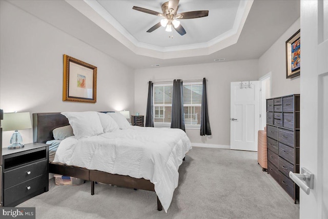 bedroom featuring light carpet, baseboards, a ceiling fan, ornamental molding, and a tray ceiling