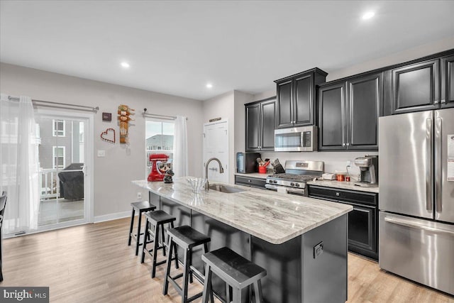 kitchen featuring an island with sink, appliances with stainless steel finishes, a breakfast bar, dark cabinets, and a sink