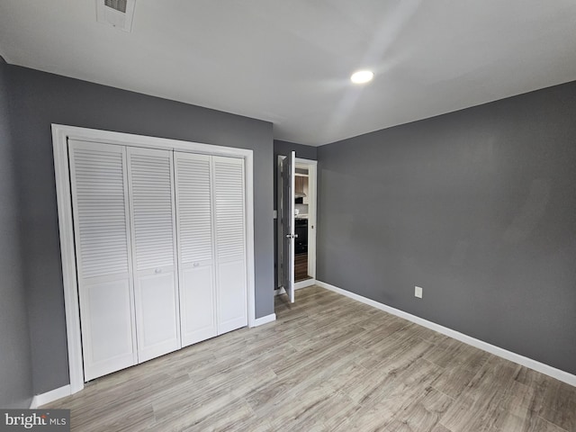 unfurnished bedroom featuring a closet, visible vents, light wood-style flooring, and baseboards