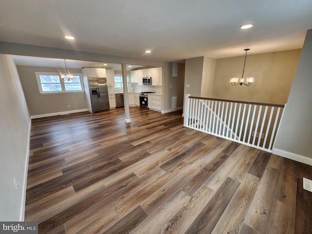 unfurnished living room with dark wood-style flooring, a notable chandelier, and baseboards