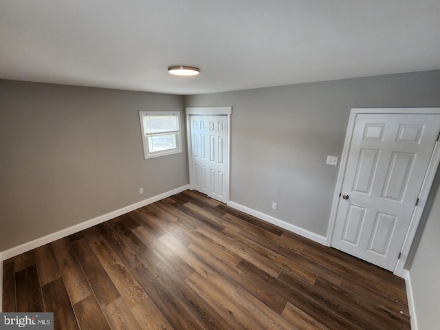 unfurnished bedroom featuring dark wood-style flooring, a closet, and baseboards