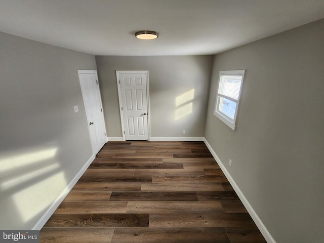 spare room featuring baseboards and dark wood-type flooring