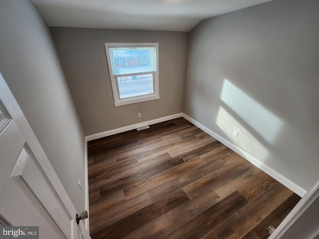 empty room with dark wood-type flooring, visible vents, and baseboards