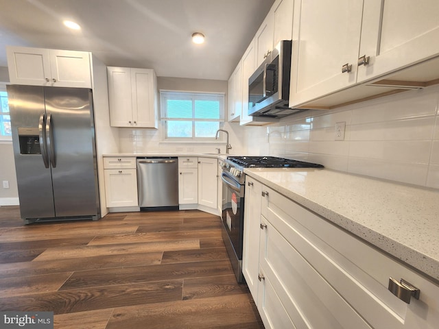 kitchen featuring light stone countertops, stainless steel appliances, dark wood-style flooring, white cabinets, and decorative backsplash