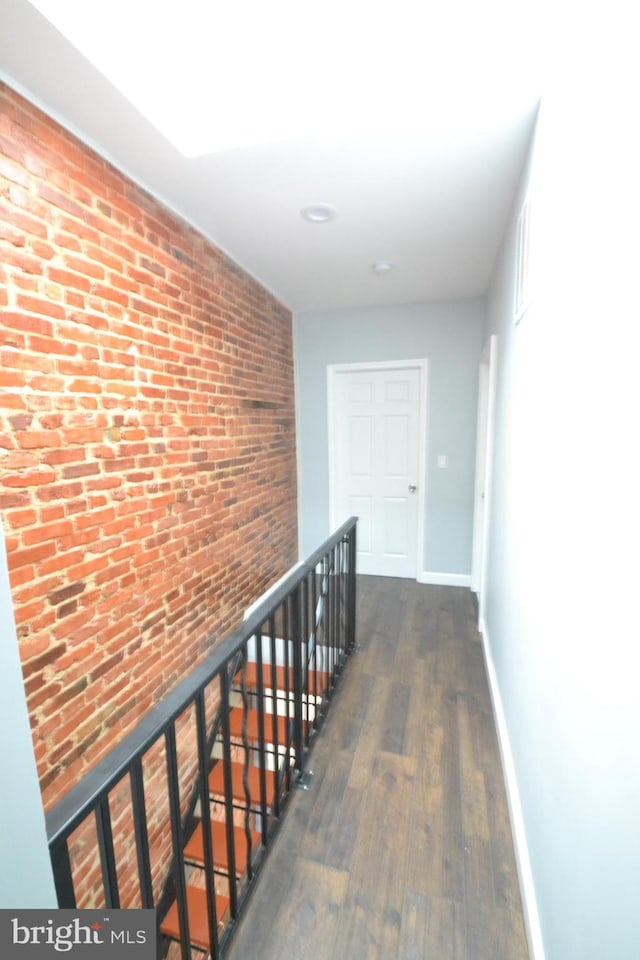 hallway featuring brick wall, dark wood-style flooring, baseboards, and an upstairs landing