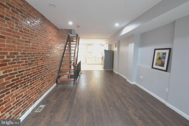 hallway with brick wall, dark wood-style flooring, and baseboards