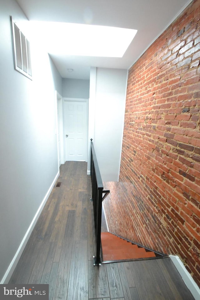 hallway with brick wall, visible vents, dark wood-style flooring, and an upstairs landing