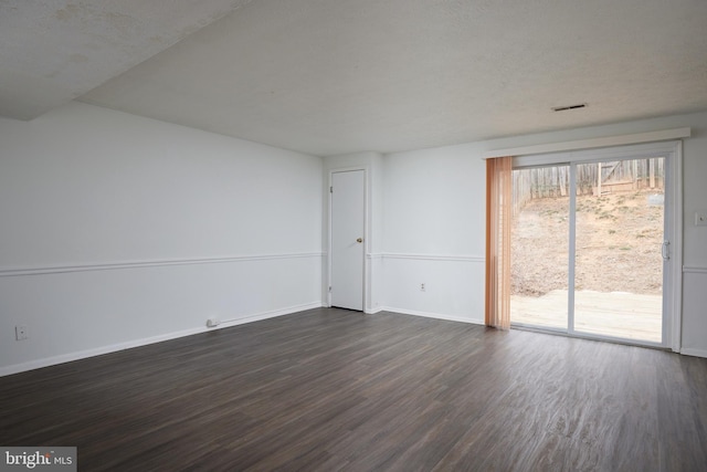 unfurnished room featuring dark wood-style flooring, visible vents, and baseboards