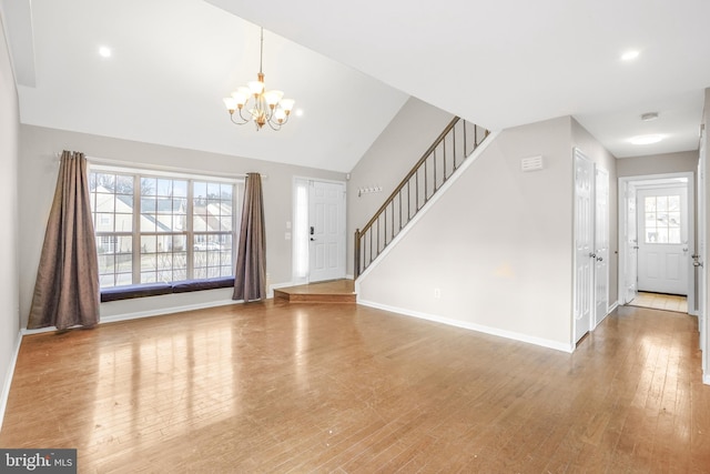 foyer entrance featuring baseboards, lofted ceiling, wood finished floors, an inviting chandelier, and stairs