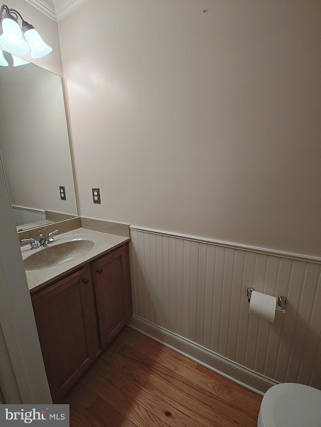 half bath featuring a wainscoted wall, toilet, wood finished floors, and vanity