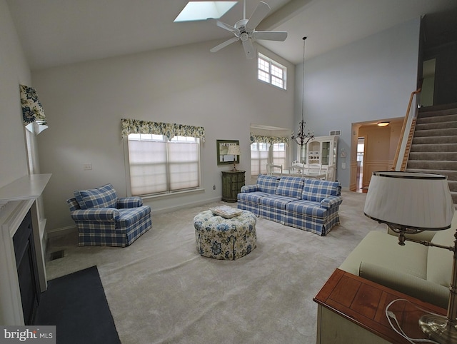 living room featuring stairs, a skylight, light carpet, baseboards, and ceiling fan with notable chandelier