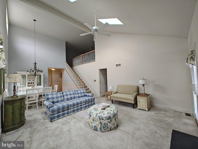 carpeted living area with ceiling fan with notable chandelier, high vaulted ceiling, stairway, and visible vents