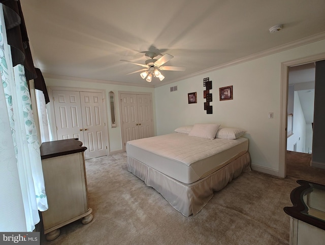 bedroom with crown molding, multiple closets, visible vents, light carpet, and ceiling fan